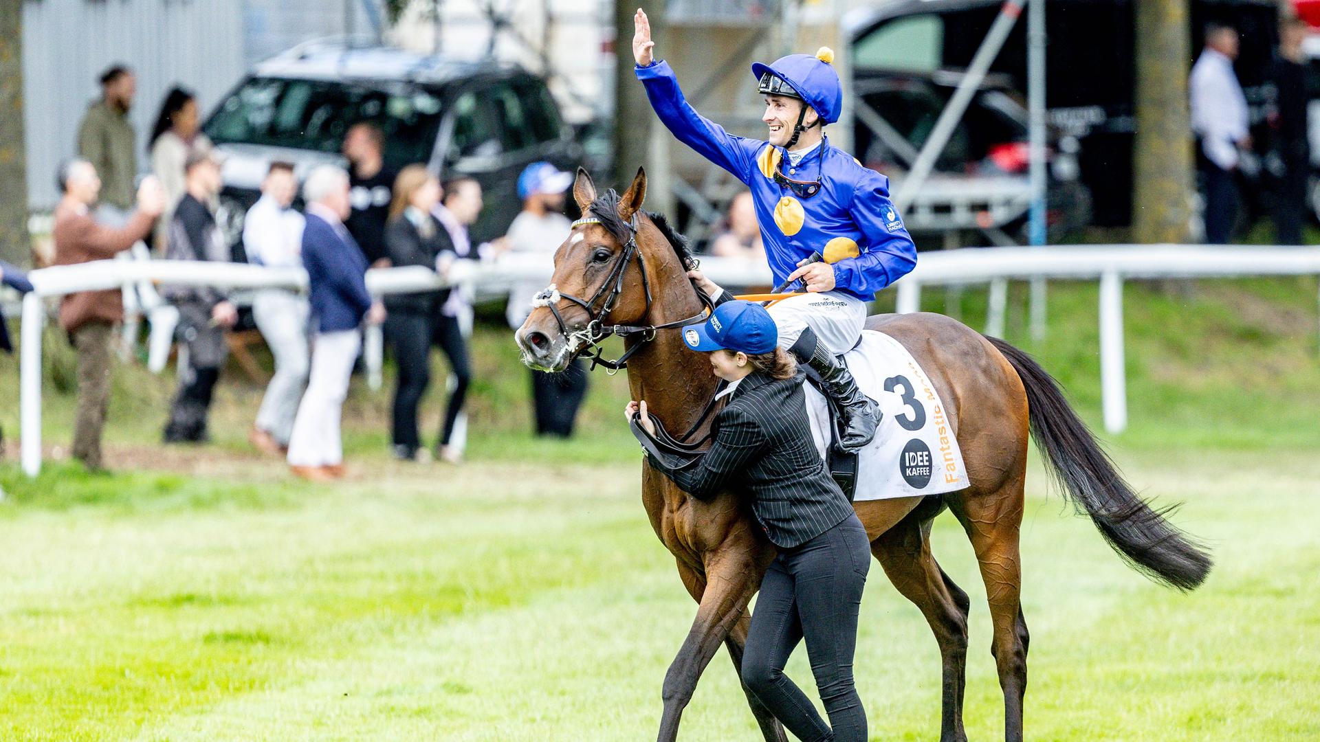 "Fantastic Moon" auf einer Rennbahn; sein Jockey im blauen Dress reist jubelnd die Arme hoch. "Fantastic Moon" auf einer Rennbahn; sein Jockey im blauen Dress reist jubelnd die Arme hoch.