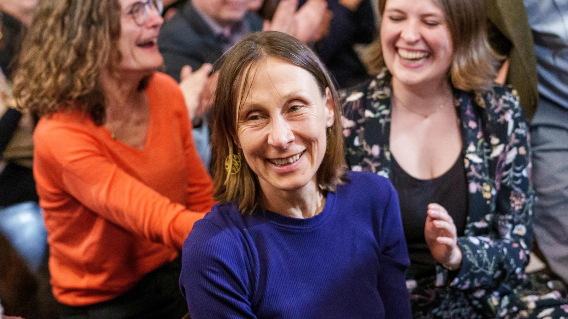 Martina Hefter erhebt sich lachend aus dem Publikum bei der Preisverleihung, die Menschen um sie herum applaudieren