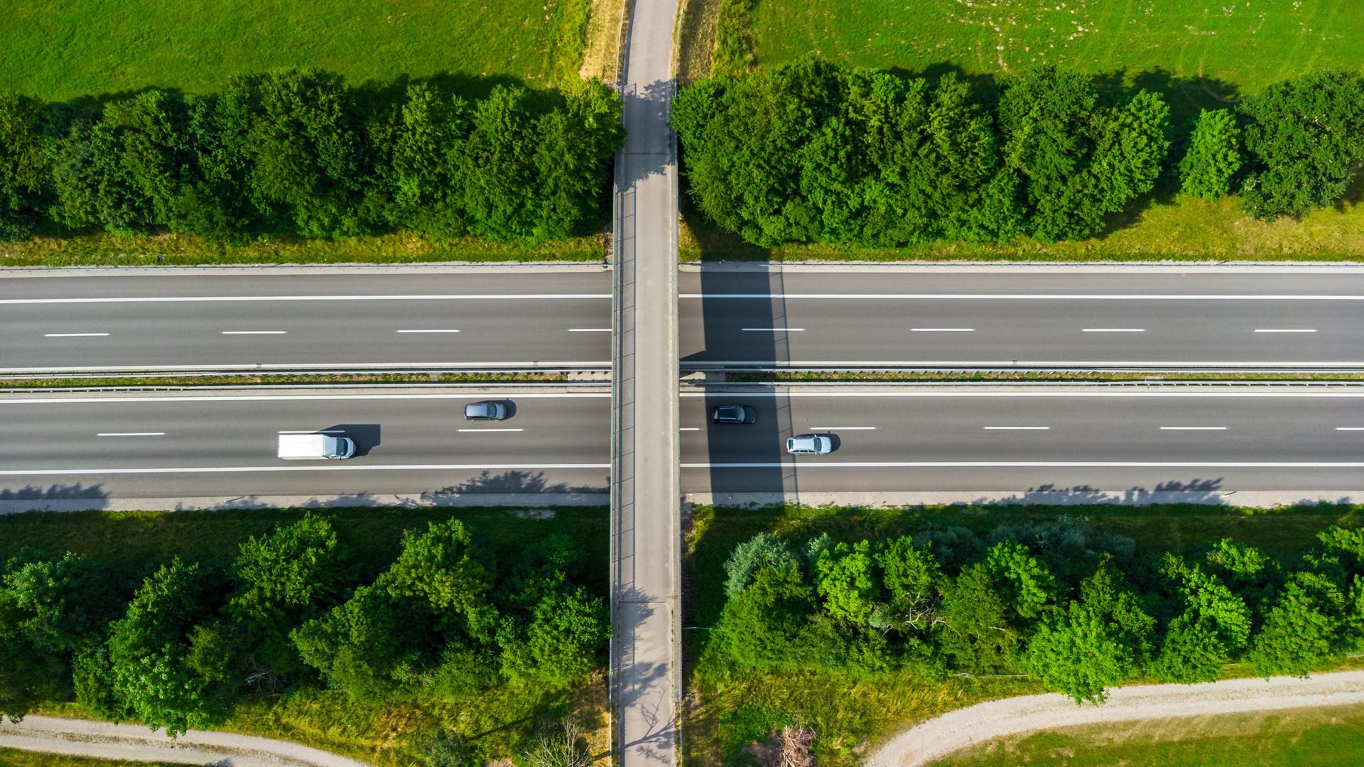 Luftaufnahme einer Brücke über einer Autobahn. Auf der Autobahn fahren vier Autos.