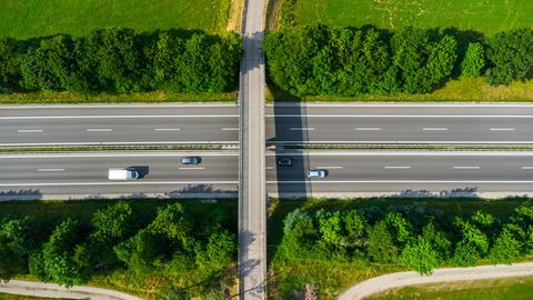 Luftaufnahme einer Brücke über einer Autobahn. Auf der Autobahn fahren vier Autos.