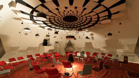 Ein futuristisch anmutender Raum in weiß mit roten Stühlen und den unterschiedlichsten hängenden, stehenden und verbauten Lautsprechern