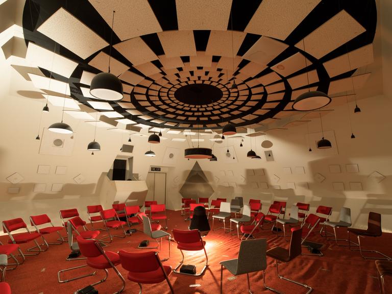 Ein futuristisch anmutender Raum in weiß mit roten Stühlen und den unterschiedlichsten hängenden, stehenden und verbauten Lautsprechern