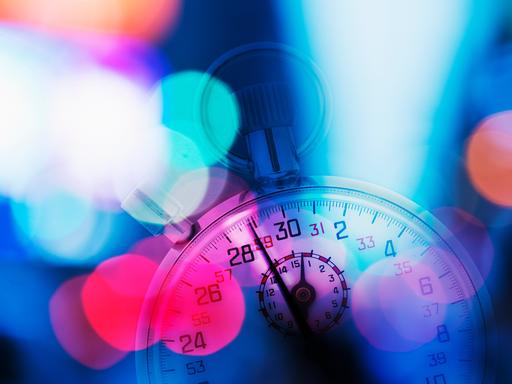 Eine Stoppuhr im Anschnitt, die leicht vor roten, blauen, violetten und pinken Lichtpunkten verschwindet