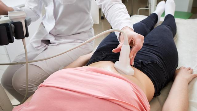 Eine Ärztin führt den Ultraschall-Scanner über den Bauch von einer Frau.
