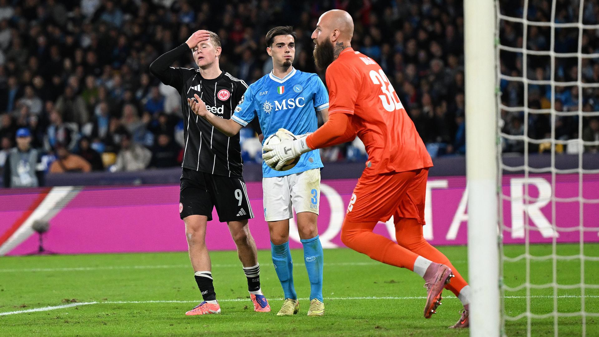 Torwart Vanja Milinkovic-Savic vom SSC Neapel ist rechts im Bild vor seinem Tor zu sehen und hält den Ball. Links steht Jonathan Burkardt von Eintracht Frankfurt hinter Miguel Gutierrez vom SSC Neapel. Burkardt hält sich mit der rechten Hand den Kopf. 