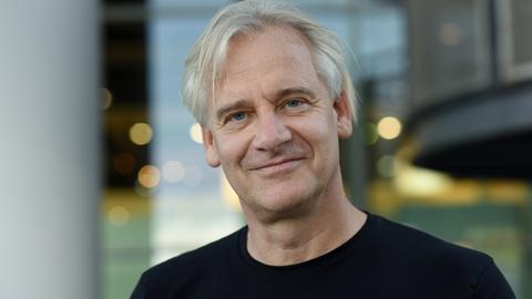 Chris Kraus lächelt in die Kamera. Er trägt ein schwarzes T-Shirt und halblanges graues Haar.