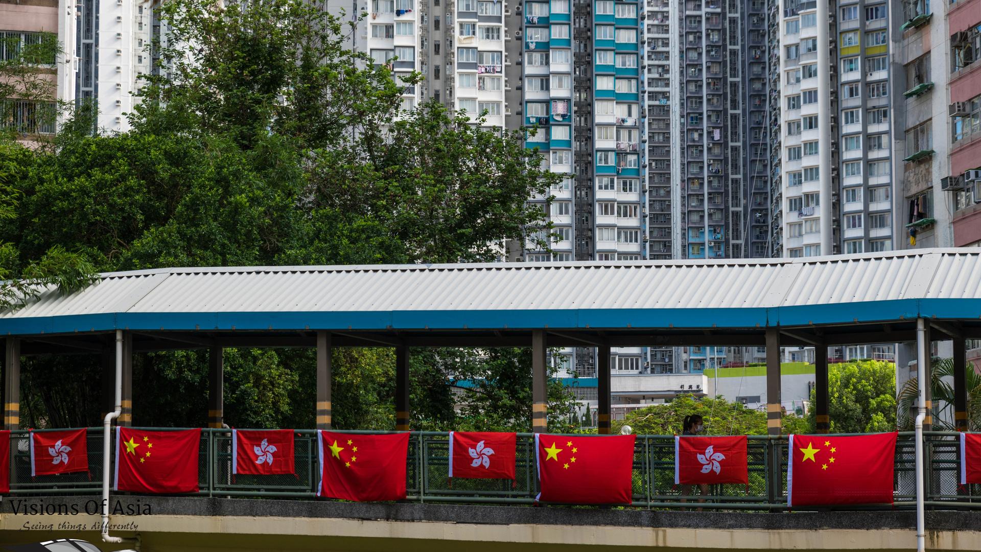 Fahnen von Hongkong und China schmücken einen Übergang in Hongkong vor dem Hintergrund von Hochhäusern.