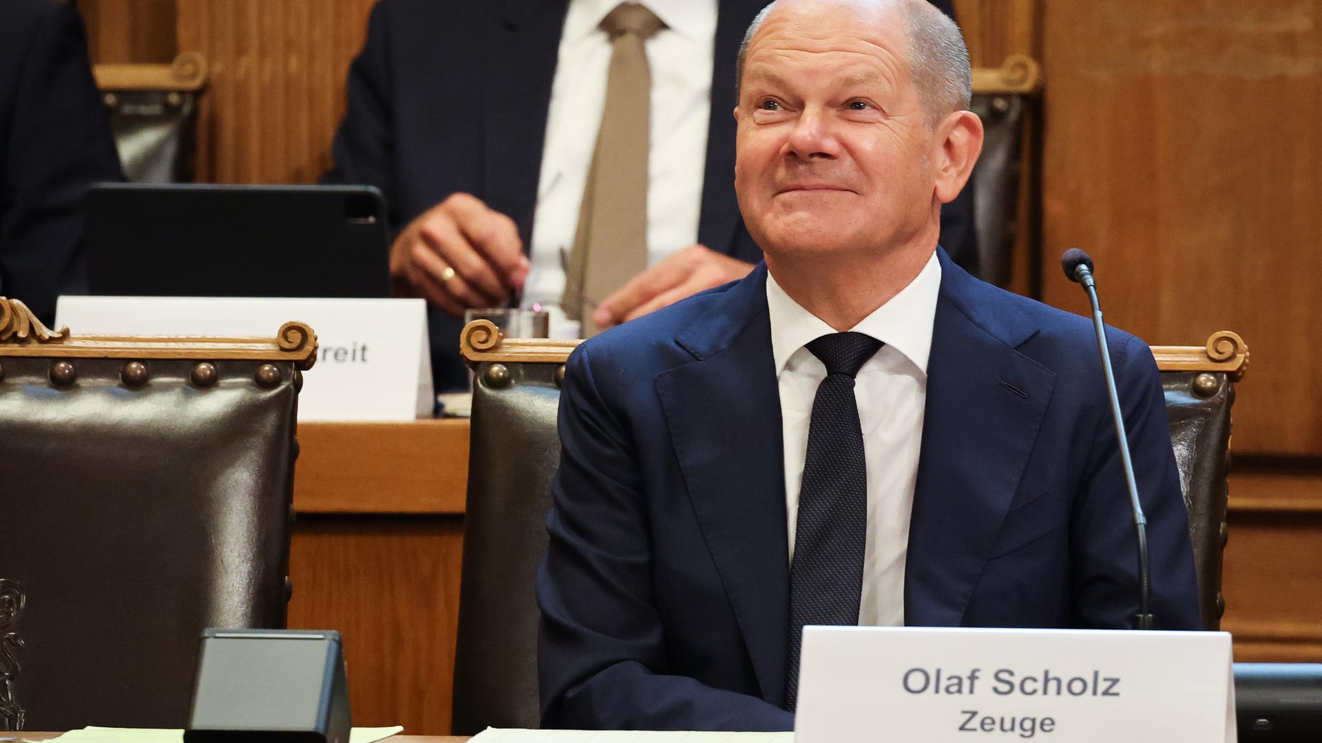 Bundeskanzler Scholz  sitzt auf seinem Platz auf der Senatsbank mit einem Plastikschild mit dem Text "Olaf Scholz Zeuge" vor Beginn einer Sitzung des Parlamentarischen Untersuchungsausschusses "Cum-Ex" im Plenarsaal der Hamburgischen Bürgerschaft im Rathaus.