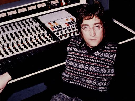 John Lennon sitzt an einer Studiokonsole aus den Siebzigern und blickt ernst in die Kamera