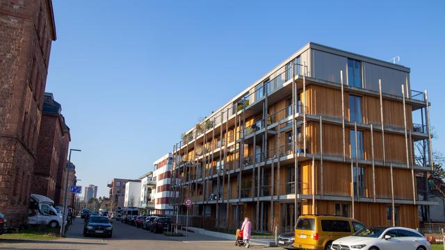 An einem neu gebauten vierstöckigen Haus in Mannheim geht eine Frau mit Kinderwagen vorbei.