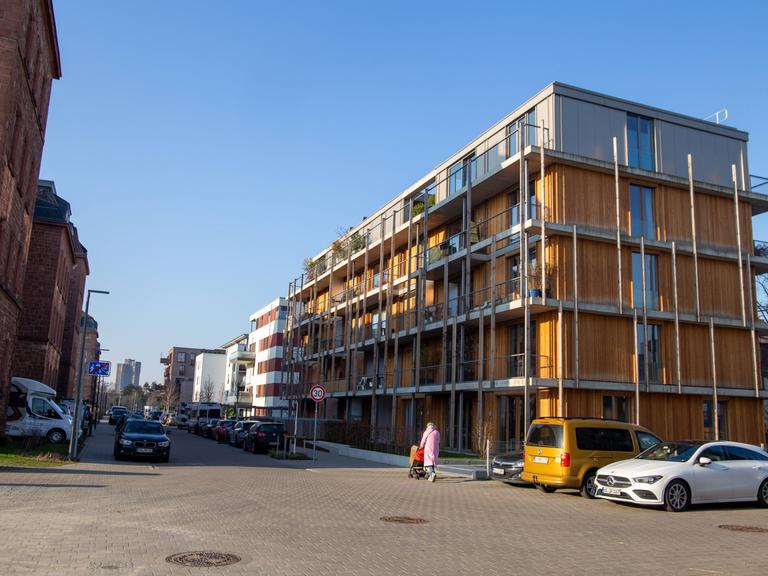 An einem neu gebauten vierstöckigen Haus in Mannheim geht eine Frau mit Kinderwagen vorbei.