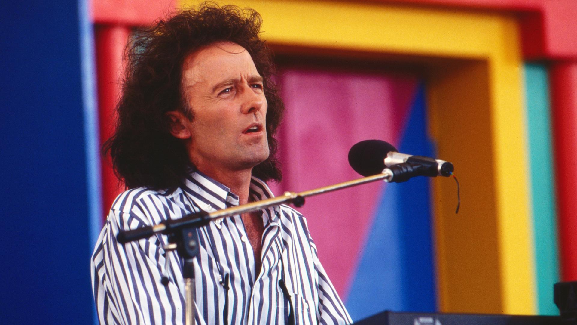 Gilbert O´Sullivan 1993 bei einem Konzert in Deutschland. Er trägt ein längsgestreiftes Hemd, die Haare trägt er schullterlang. 