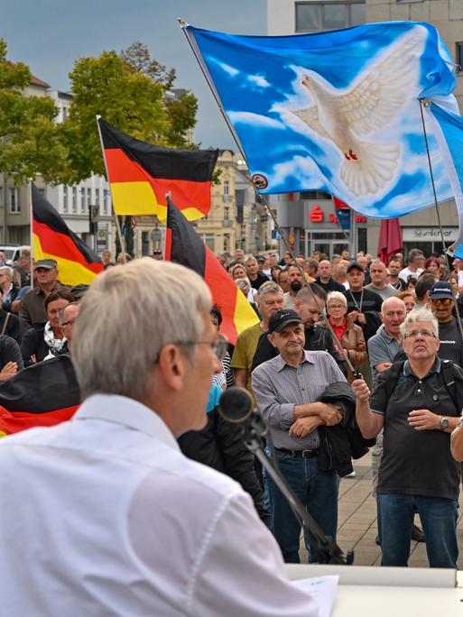 Hans-Christoph Berndt, Fraktionsvorsitzender der AfD im brandenburgischen Landtag, spricht auf der Demonstration von "Zukunft Heimat". Zu sehen sind Fahnen mit Friedenstaube und die Deutschlandfahne.