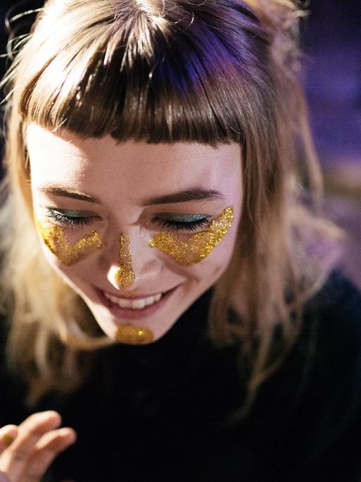 Eine junge Frau trägt goldenes Glitzer-Makeup im Gesicht