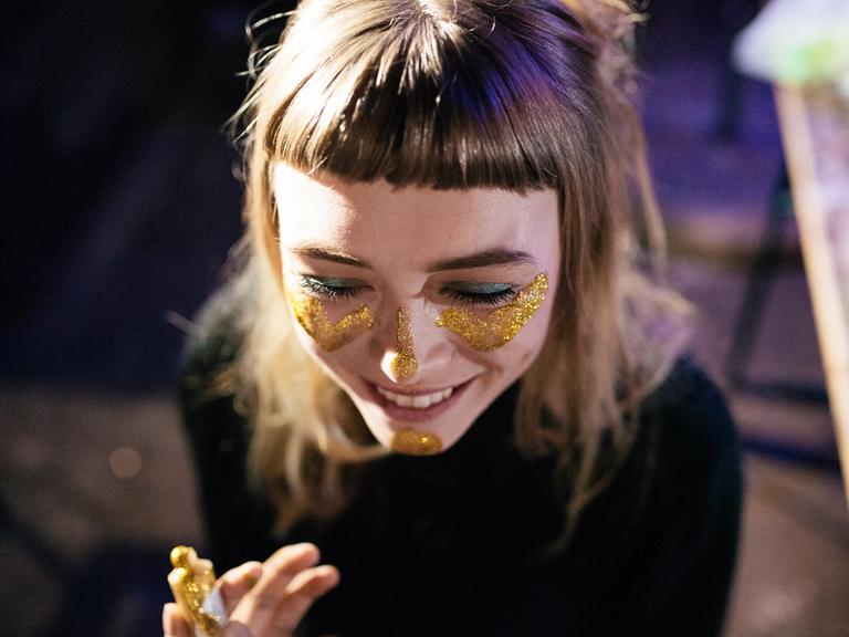 Eine junge Frau trägt goldenes Glitzer-Makeup im Gesicht