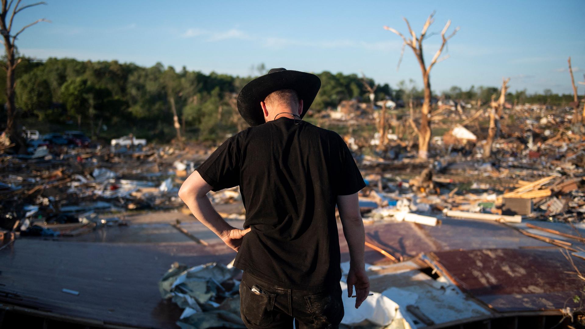 Ein Mann mit schwarzem Cowboyhut steht mit gesenktem Kopf vor den Überresten eines durch Tornados zerstörten Gebäudes. Ein Mann mit schwarzem Cowboyhut steht mit gesenktem Kopf vor den Überresten eines durch Tornados zerstörten Gebäudes.