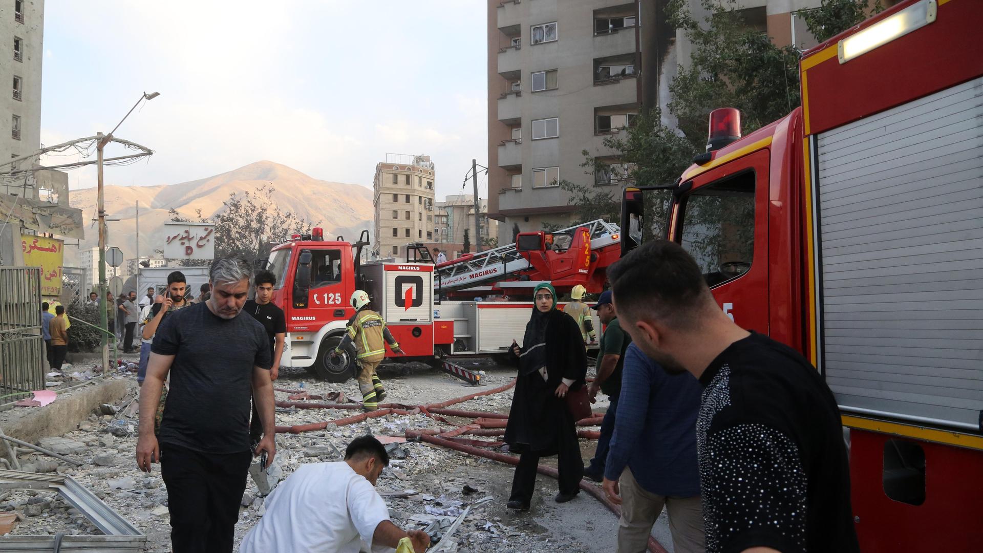 Feuerwehrwagen und Menschen vor zerstörtem Gebäude in Teheran (Iran), das bei einem israelischen Luftangriff getroffen wurde (13.6.2025) 
