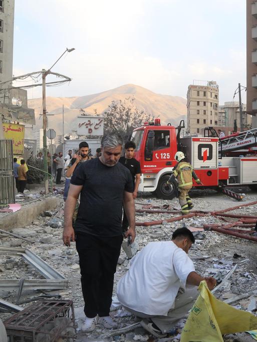 Feuerwehrwagen und Menschen vor zerstörtem Gebäude in Teheran (Iran), das bei einem israelischen Luftangriff getroffen wurde (13.6.2025) 