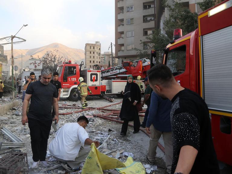 Feuerwehrwagen und Menschen vor zerstörtem Gebäude in Teheran (Iran), das bei einem israelischen Luftangriff getroffen wurde (13.6.2025) 