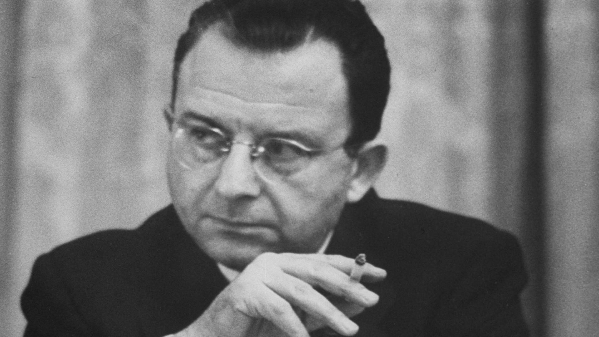 Erich Fromm raucht im Sitzen und hört zu.