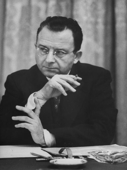 Erich Fromm raucht im Sitzen und hört zu.