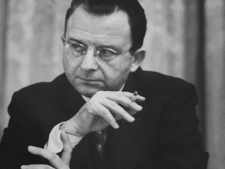 Erich Fromm raucht im Sitzen und hört zu.