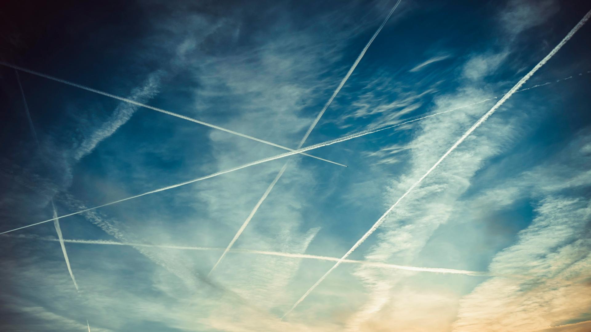 Blick in den Himmel, wo im Gegenlicht Flugzeuge mit Kondensstreifen zu sehen sind Blick in den Himmel, wo im Gegenlicht Flugzeuge mit Kondensstreifen zu sehen sind