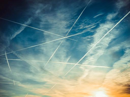 Blick in den Himmel, wo im Gegenlicht Flugzeuge mit Kondensstreifen zu sehen sind