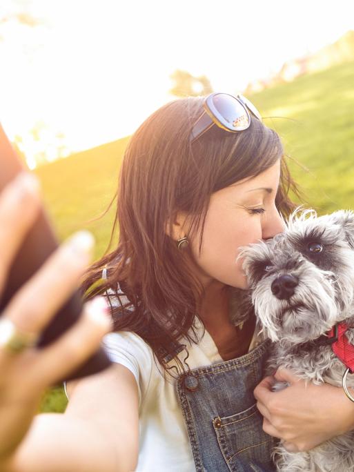Eine junge Frau hält einen Hund im Arm und macht ein Foto mit einem Smartphone.