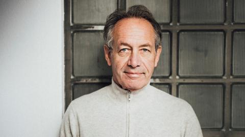 Robert Hunger-Bühler steht in einem beigen Pullover an eine Glassteinwand gelehnt