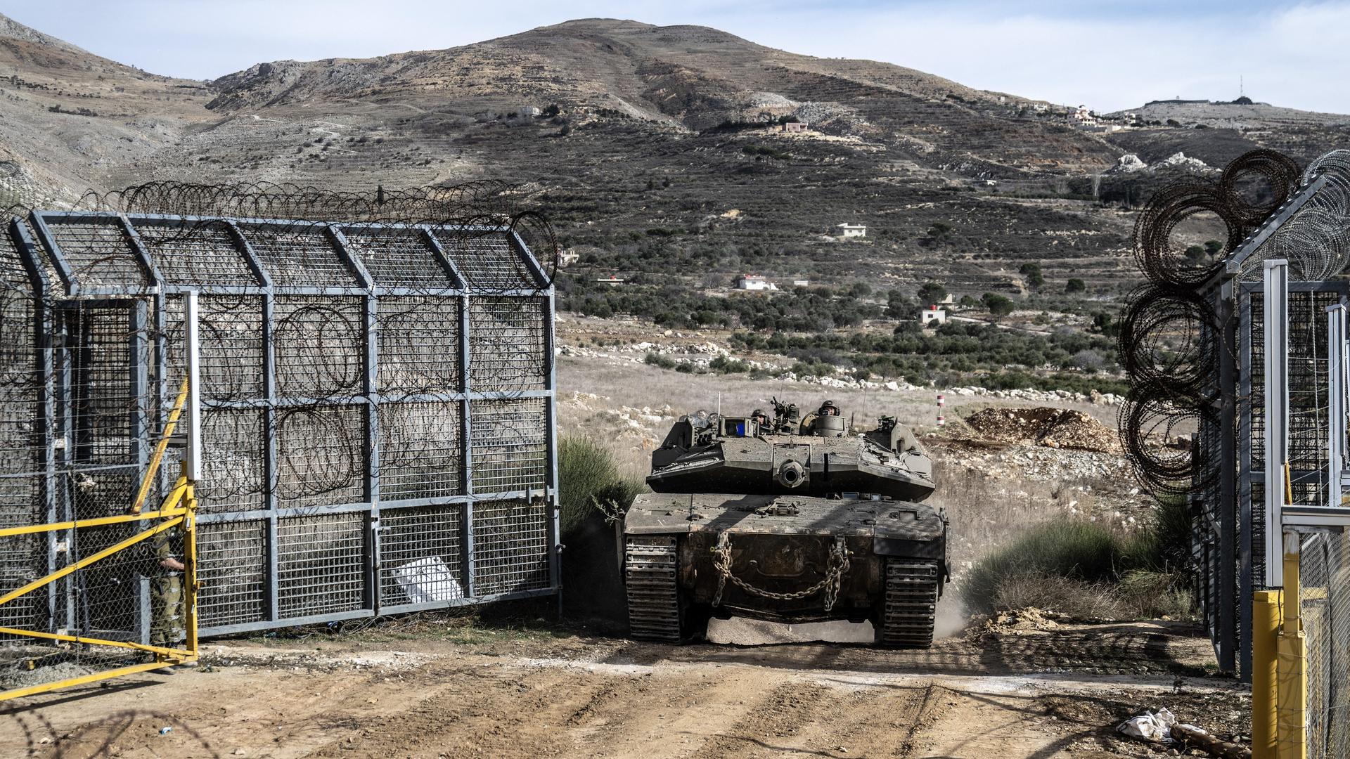 Israelische Panzer passieren einen Grenzzaun in der Region der Golanhöhen, im Hintergrund sind Berge zu sehen.