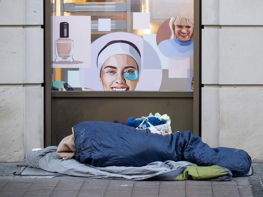 Ein Obdachloser schläft auf seinem Lager im Frankfurter Bahnhofsviertel vor einem Kosmetikgeschäft.