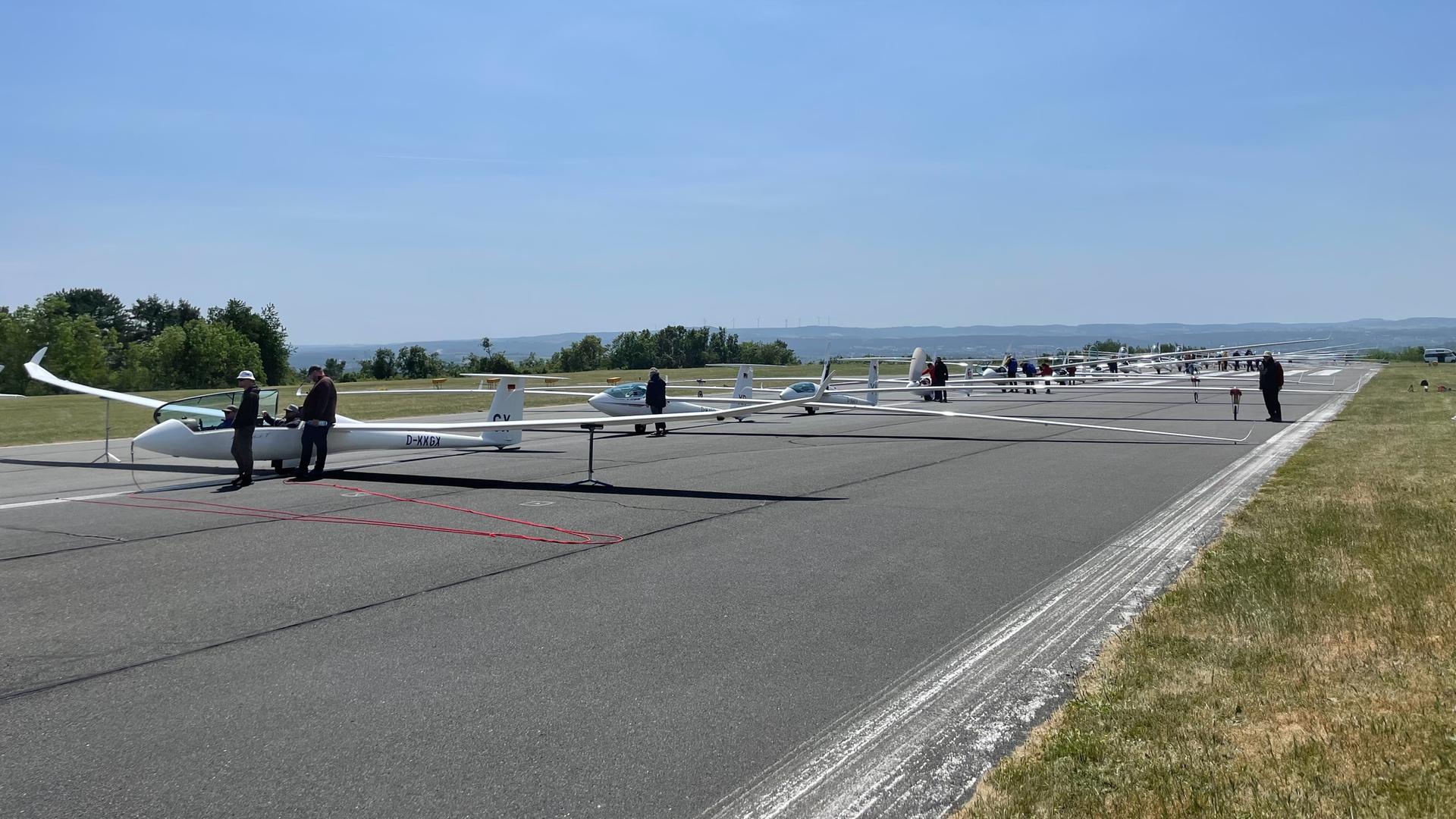 Viele Segelflugzeuge stehen in einer Reihe auf der Startbahn.