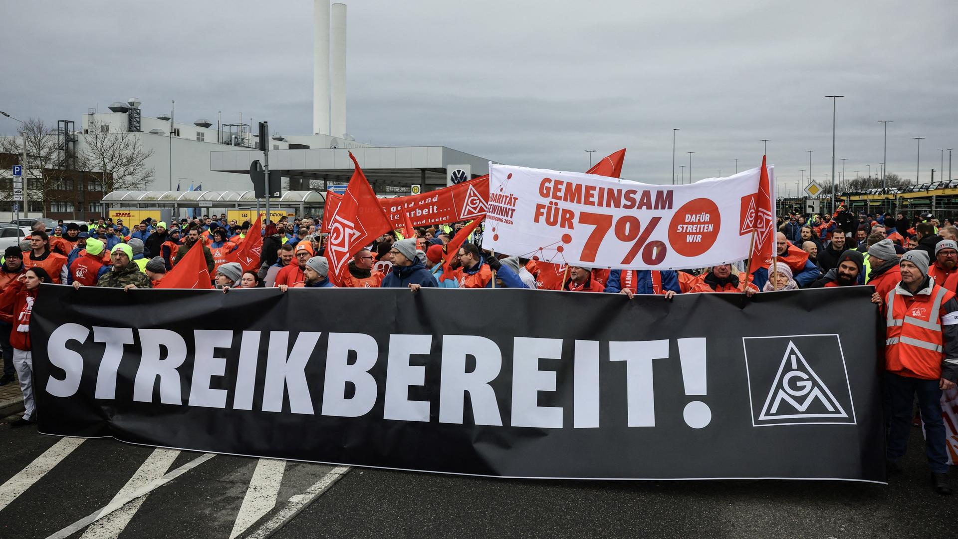 Die Mitarbeiter halten ein schwarzes Banner mit der weißen Aufschrift "Streikbereit!" vor sich. Viele tragen rote Warnwesten. 