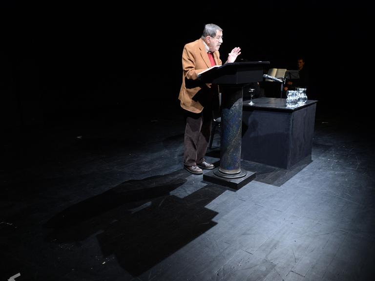 Der Schriftsteller Günter Grass steht auf einer Bühne vor einem Stehpult und liest aus einem Buch vor. 