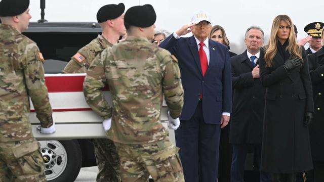 Donald Trump salutiert, während Soldaten einen in die US-Flagge gehüllten Sarg an ihm vorbeitragen.