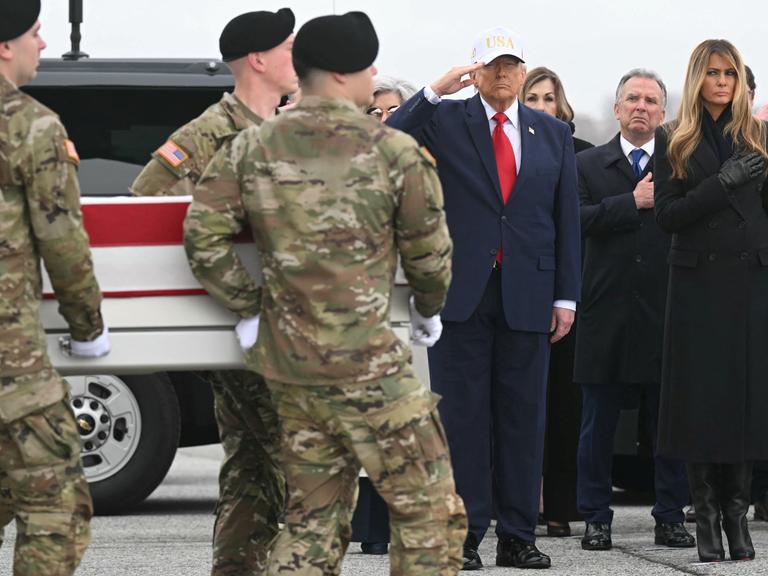 Donald Trump salutiert, während Soldaten einen in die US-Flagge gehüllten Sarg an ihm vorbeitragen.