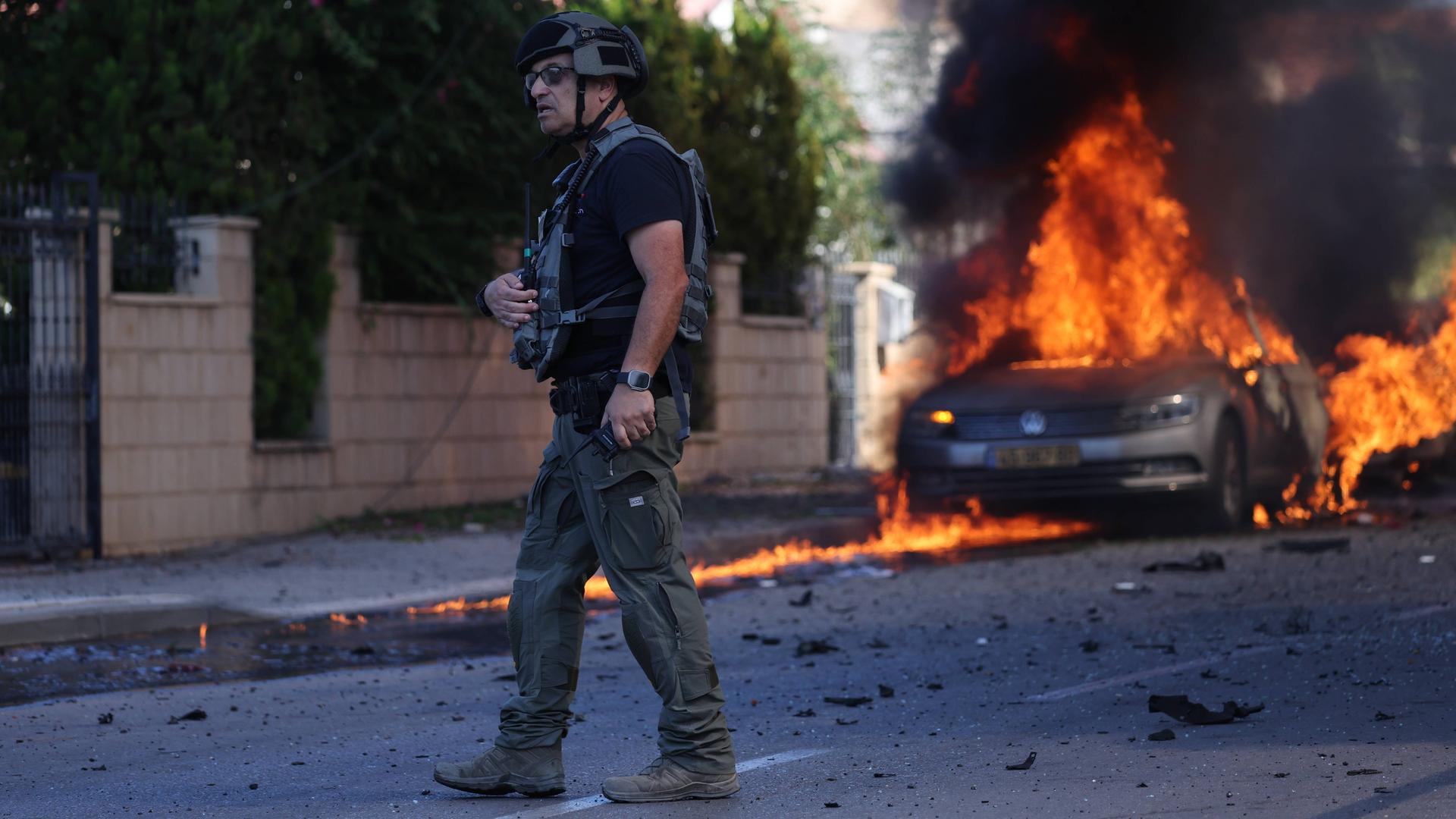 Ein israelischer Polizist vor einem brennenden Auto in Ashkelon.