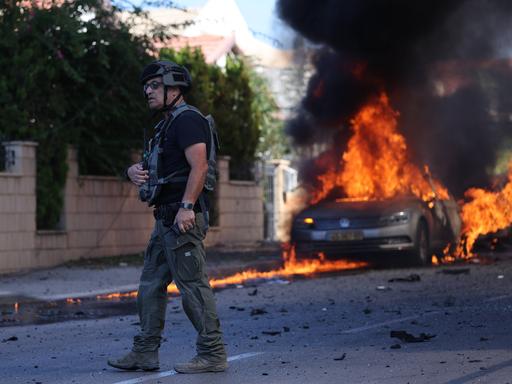 Ein israelischer Polizist vor einem brennenden Auto in Ashkelon.
