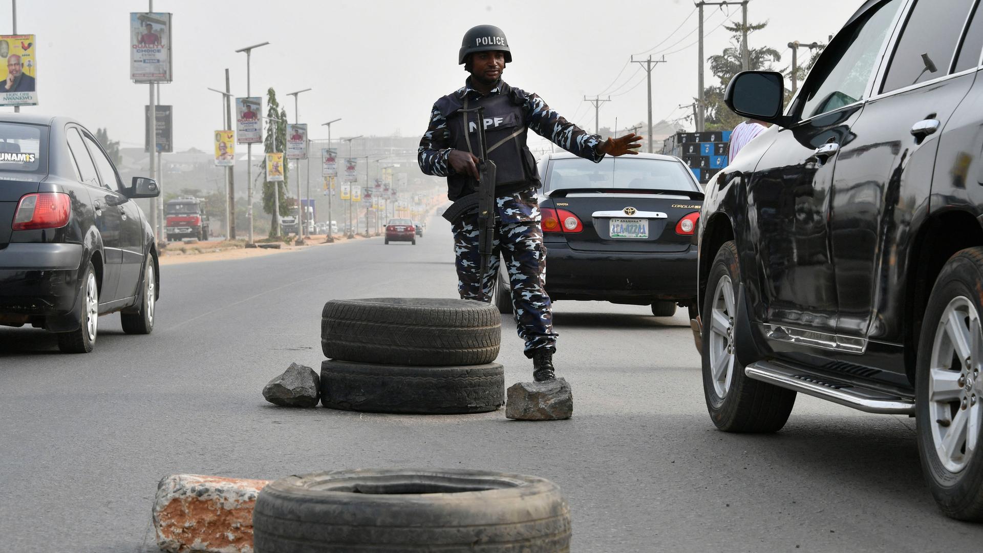Ein schwer bewaffneter Polizist steht in der Mitte einer breiten Straße und hält ein Auto an.