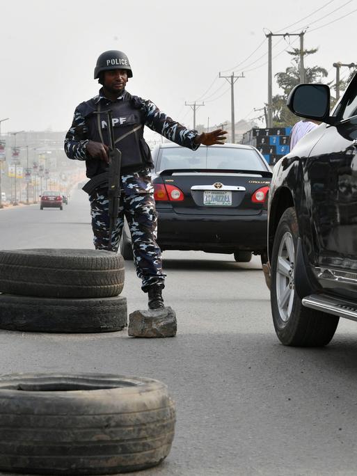 Ein schwer bewaffneter Polizist steht in der Mitte einer breiten Straße und hält ein Auto an.