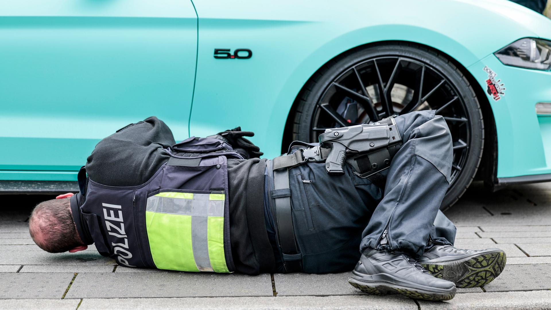 Ein Polizist liegt auf dem Boden und schaut unter einen türkisfarbenen Sportwagen. Ein Polizist liegt auf dem Boden und schaut unter einen türkisfarbenen Sportwagen.