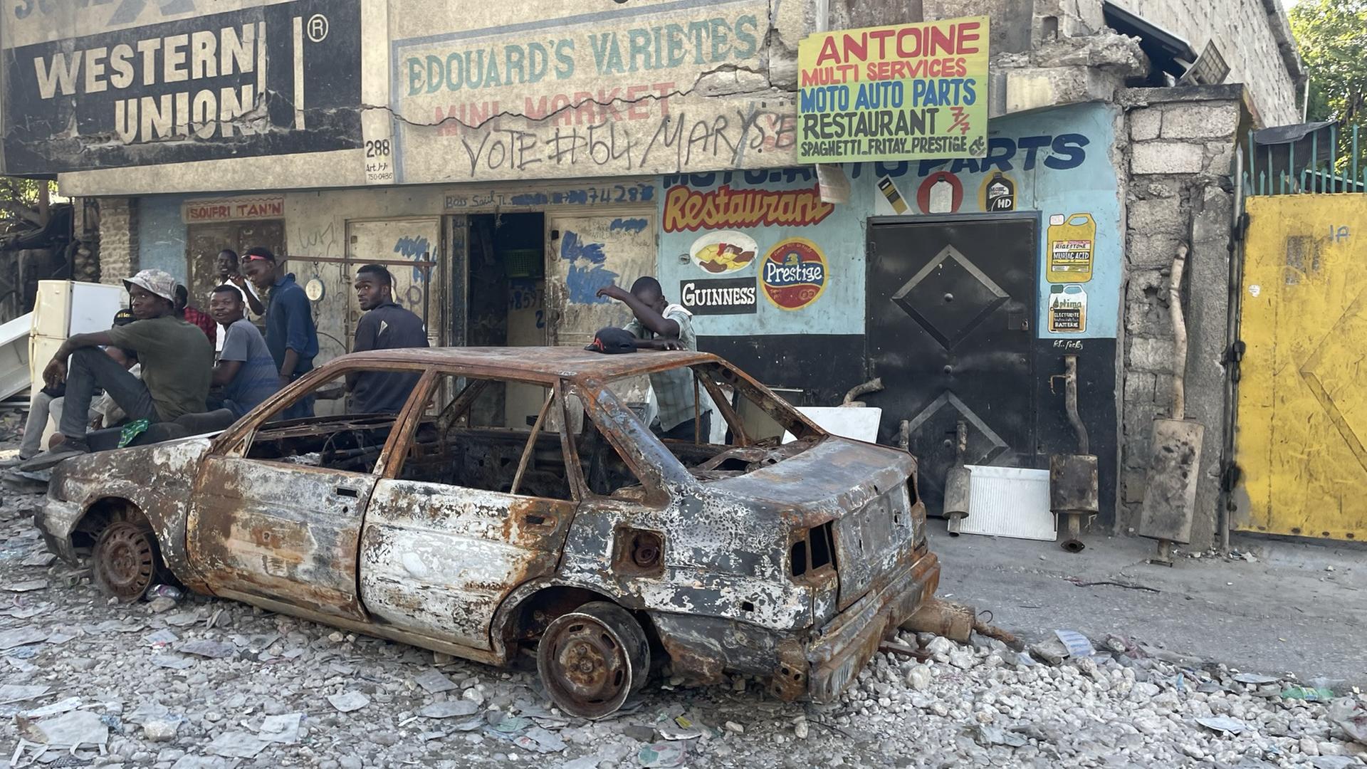 Auf einem ausgebrannten Auto in einer zerstörten Straße im Viertel Feuilles de Carrefour sitzen jungen Männer.