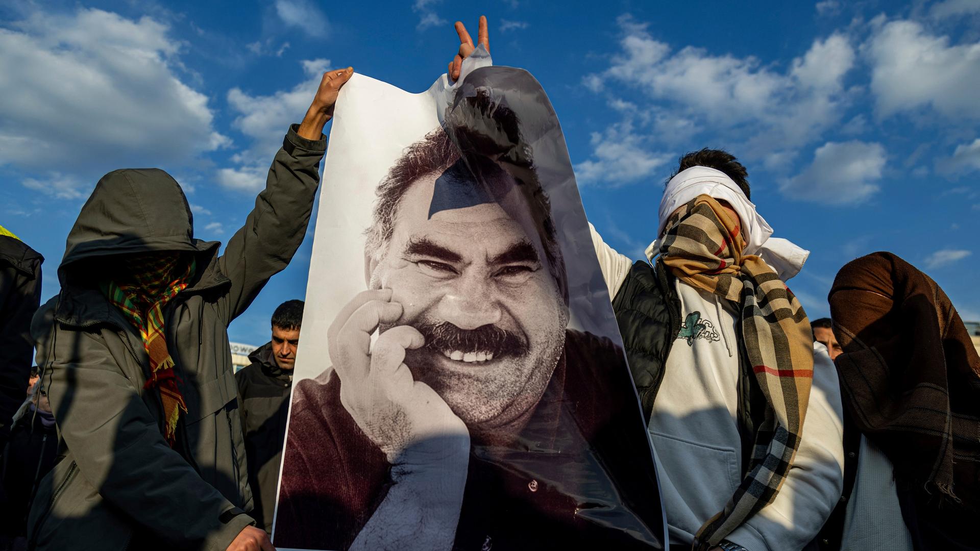 Zwei Männer, deren Gesichter verühhlt sind, halten ein Plakat mit PKK-Führer Abdullah Öcalan in die Höhe