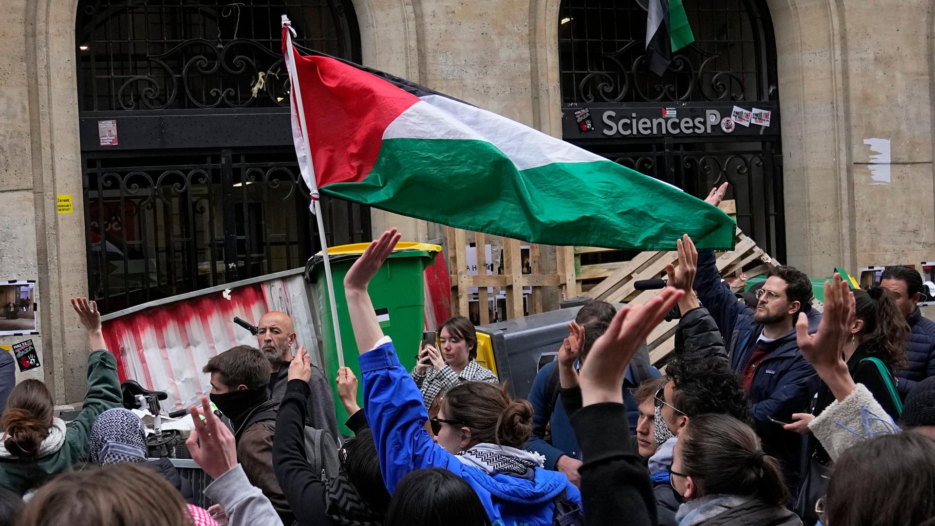 Demonstranten blockieren ein Gebäude der Universität Scienes Po in Paris. Sie tragen eine palästinensische Flagge und haben Barrikaden vor dem eingang errichtet.