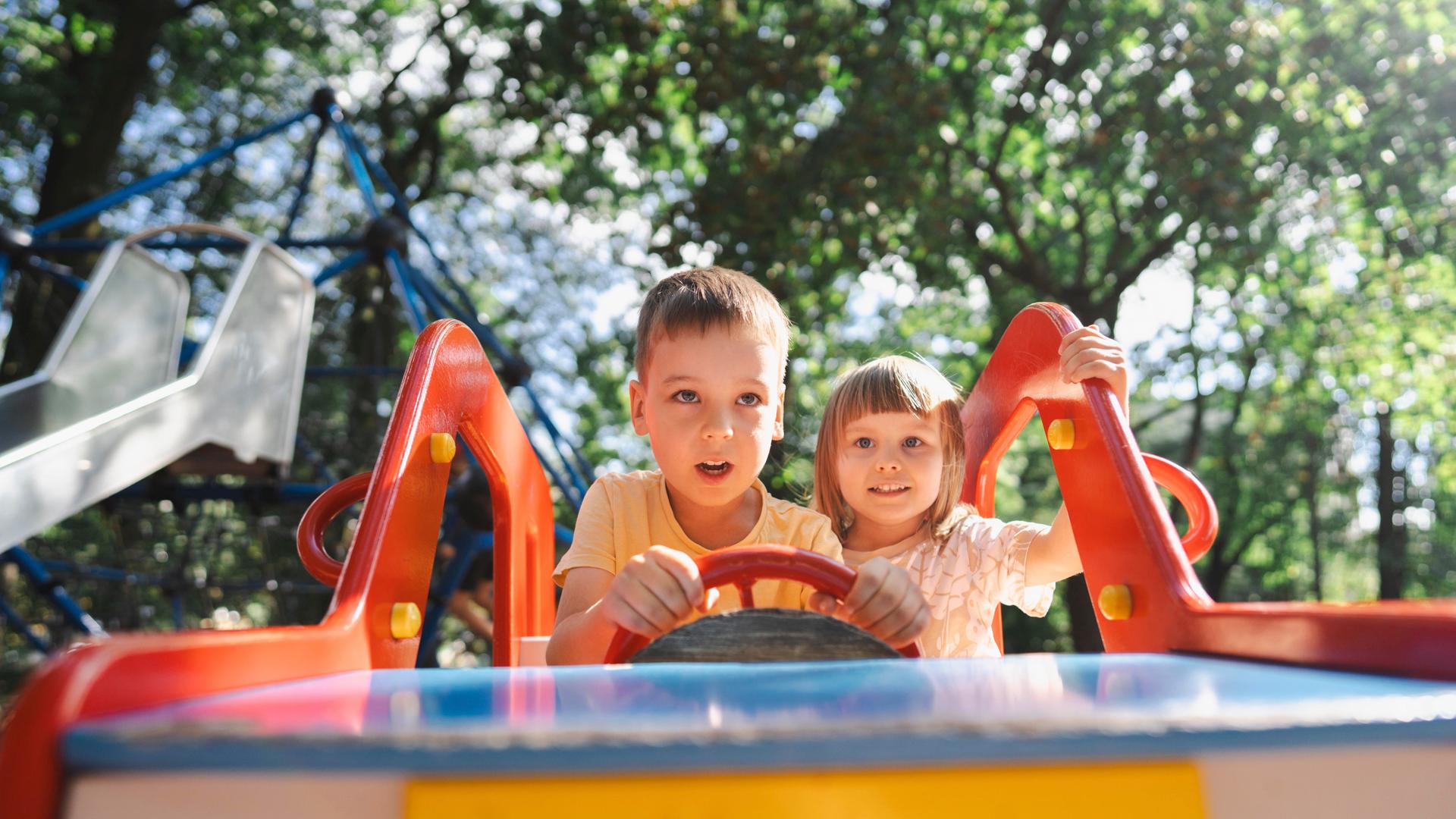 Ein Junge und ein Mädchen sitzen auf einem Spielplatz in einem Spielauto