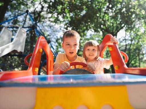 Ein Junge und ein Mädchen sitzen auf einem Spielplatz in einem Spielauto