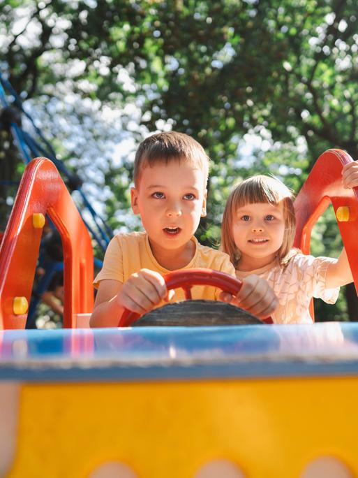 Ein Junge und ein Mädchen sitzen auf einem Spielplatz in einem Spielauto