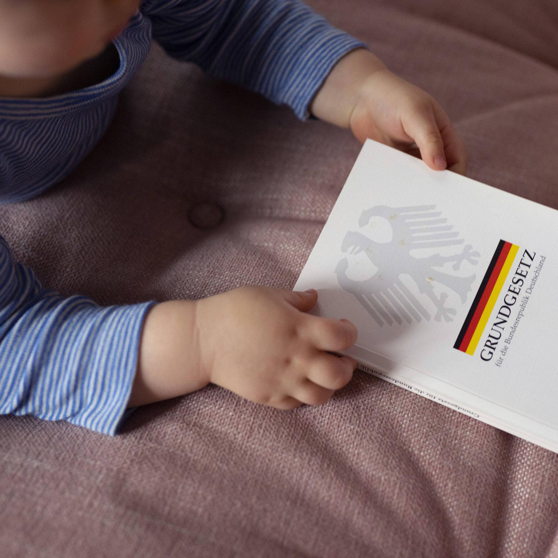 Ein Kleinkind hält ein deutsches Grundgesetz in der Hand.