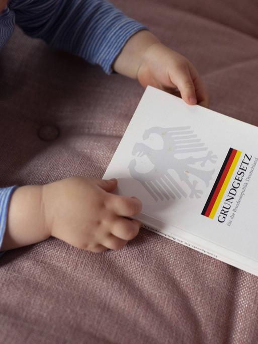 Ein Kleinkind hält ein deutsches Grundgesetz in der Hand.